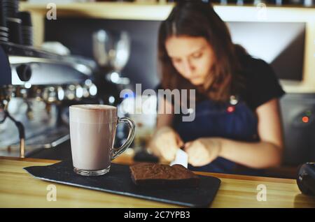 Barista macht rosa Matcha Latte mit Milch. Der Barkeeper bereitet leckere Drinks und Brownie-Kuchen zu Stockfoto