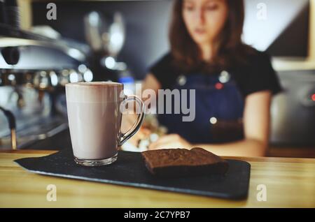 Barista macht rosa Matcha Latte mit Milch. Der Barkeeper bereitet leckere Drinks und Brownie-Kuchen zu Stockfoto