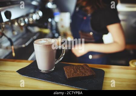 Barista macht rosa Matcha Latte mit Milch. Der Barkeeper bereitet leckere Drinks und Brownie-Kuchen zu Stockfoto