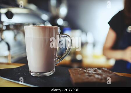 Barista macht rosa Matcha Latte mit Milch. Barkeeper bereitet leckere Getränke und Brownie Cake.Blurred Bild, selektiver Fokus Stockfoto