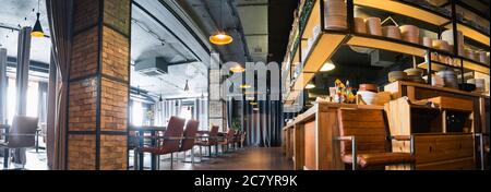 Halb beleuchtete Halle im Loft-Stil in einem mexikanischen Restaurant mit offener Küche im Hintergrund. Vor der Küche gibt es Holztische mit mu Stockfoto