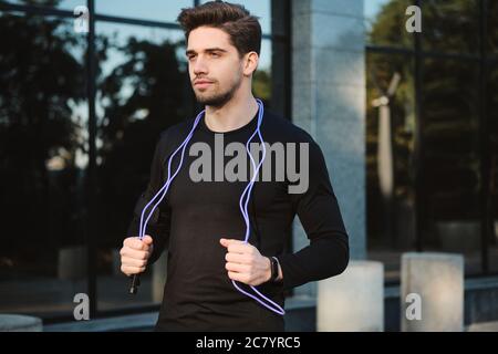 Seitenansicht des jungen sportlichen Mannes mit Springseil nachdenklich Blick weg auf Workout im Freien Stockfoto