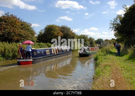 Zwei schmale Boote, die im Hochsommer auf dem Kennet & Avon Canal in Wiltshire, England, vorbeifahren, mit Wanderern auf dem Schleppweg. Stockfoto