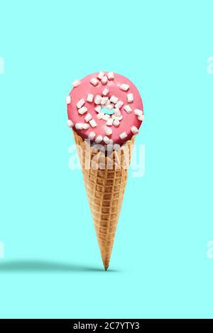 Süßer Donut glasiert von rosa Vereisung bestreut mit Marshmallow in Wafer-Kegel auf türkisfarbenem Hintergrund. Leckereien, ungesunde Ernährung. Nahaufnahme, Kopierbereich Stockfoto