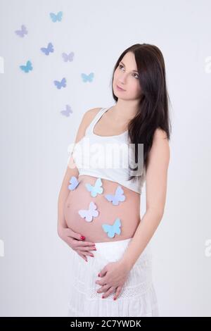 Junge schwangere Frau mit bunten Schmetterlingen auf dem Bauch über weißem Hintergrund Stockfoto