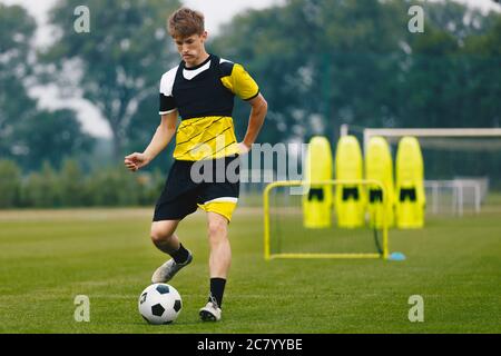 Junge Teenager-Fußballspieler auf Trainingsfeld tritt Fußball. Jugendsportler läuft auf Rasen. Junge in Fußballschuhen und Fußballuniform Stockfoto