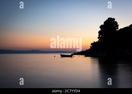 Ein herrlicher orange-blauer Abendhimmel spiegelt sich nach Sonnenuntergang im glatten Meer, auf dem ein kleines Motorboot an einer Boje liegt. Stockfoto