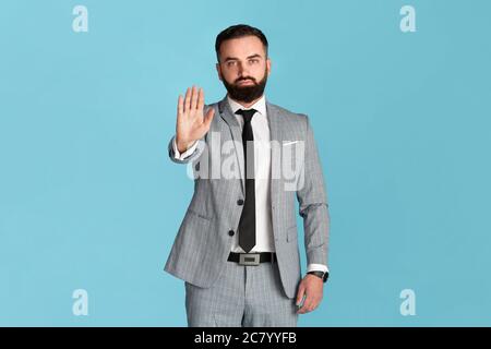 Ablehnung ausdrücken. Selbstbewusster Unternehmer in formalwear zeigt STOP-Geste auf blauem Hintergrund Stockfoto
