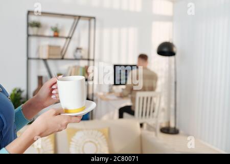 Frau bringt Tasse leckeren Kaffee zu Ehemann, der auf Programmierung Code im Hintergrund arbeitet Stockfoto