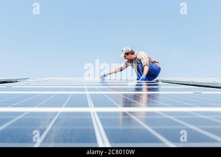 Solarpanel Energie. Elektroingenieur Mann arbeitet in Solaranlage auf dem Dach gegen blauen Himmel mit Geräten. Entwicklung Sonne alternative Energie Stockfoto