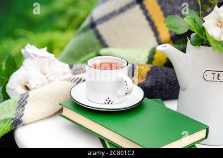 Sommer-Frühstück im Garten. Tasse Tee auf Büchern mit grünen warmen Karabell, Frühlingsblumen auf weißem Tisch im Freien. Stockfoto