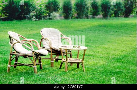 Zwei Sessel, Holzgartenmöbel auf Rasen im Freien zum Entspannen an heißen Sommertagen. Gartenlandschaft mit zwei Stühlen in der Natur. Ruhe im Park Stockfoto
