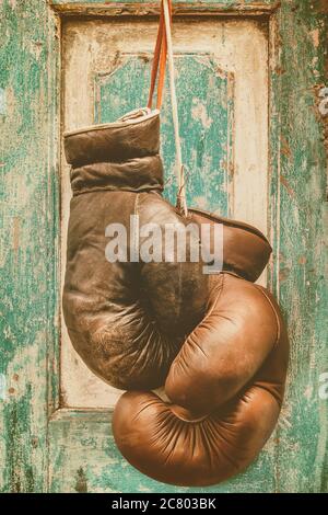 Ein Paar Vintage Boxhandschuhe, die an einer verwitterten grünen alten Holztür hängen Stockfoto