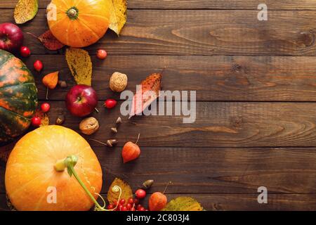Herbstkomposition. Kürbisse, gefallene Blätter, Äpfel, rote Beeren, Walnüsse auf Holztisch. Happy Thanksgiving Konzept. Flach liegend, Draufsicht, Kopierbereich Stockfoto