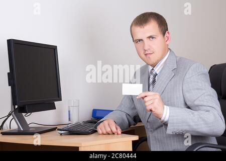 Junger Geschäftsmann sitzt im Büro und zeigt seine Visitenkarte Stockfoto