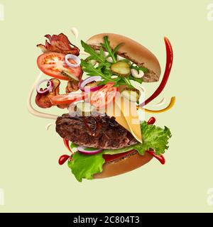 Appetitlich großer Burger mit fliegenden Zutaten vor hellgrünem Hintergrund. Schinken, Rinderschnitzel, Käse, Saucen, Gemüse und Gemüse. Nahaufnahme Stockfoto