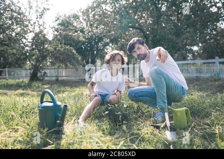 Dunkelhaariger Mann und sein Sohn sitzen auf dem Gras, Vater zeigt etwas Stockfoto