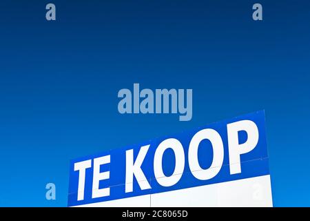 Großes Immobilienschild mit dem niederländischen Text "zum Verkauf" vor einem klaren blauen Himmel Stockfoto