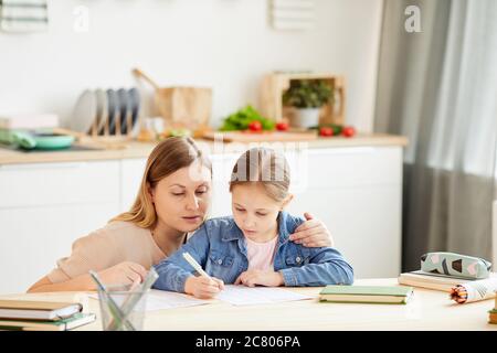 Warm-toned Porträt der fürsorglichen Mutter helfen kleinen Mädchen Hausaufgaben oder Studie am Tisch in gemütlichen Haus Innenraum, kopieren Raum Stockfoto