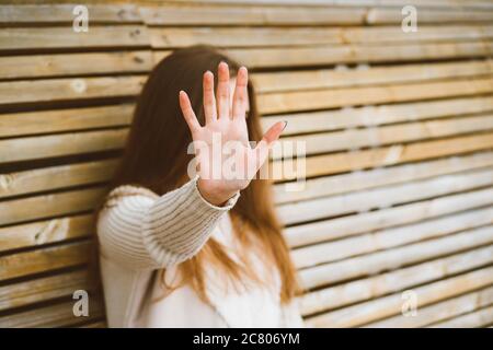 Frau mit langen Haaren reicht nach vorne und schützt ihr Gesicht vor der Kamera. Konzept der Privatsphäre, persönlicher Raum, Verbot der Fotografie. Eine Frau sitzt darauf Stockfoto