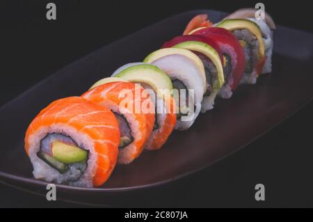 Sushi-Rolle Lachs und andere Fische schneiden und mit dunklem Hintergrund servieren. Stockfoto