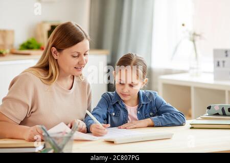 Warm-toned Porträt der fürsorglichen Mutter helfen niedlichen Mädchen Hausaufgaben und zu Hause in gemütlichen Innenraum studieren Stockfoto