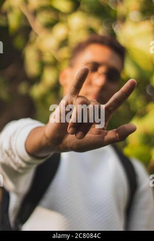 Vertikale Aufnahme eines jungen Mannes in einem Park zeigt Ein Liebeszeichen mit seiner Hand Stockfoto