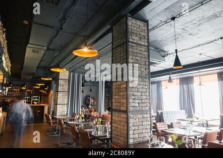Halb beleuchtete Halle im Loft-Stil in einem mexikanischen Restaurant mit offener Küche im Hintergrund. Vor der Küche gibt es Holztische mit mu Stockfoto