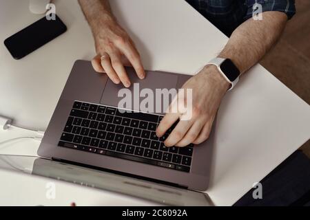 Mann Hände arbeiten auf seinem Laptop zu Hause. Home Office, Smart Watch am Handgelenk, Finger auf der Tastatur Stockfoto