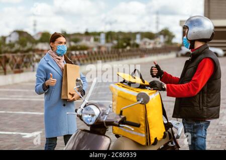 Lieferung Kurier Und Frau In Schutzmasken Gestikulierenden Daumen-Up Draußen Stockfoto
