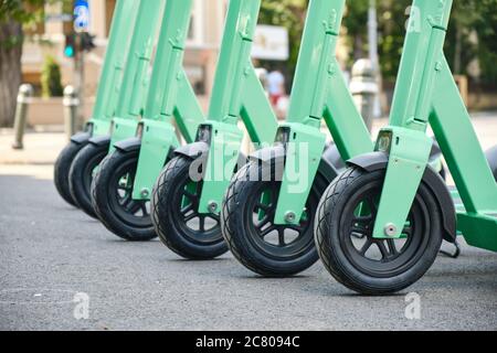 Reihe von grün-blauen Elektro-Scooter, eine saubere, moderne alternative Transportmöglichkeit in Städten. Nahaufnahme der Vorderräder. Stockfoto