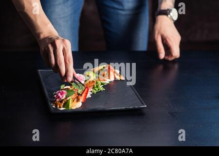 Der männliche Koch serviert köstliche Steaks auf dem Schneidebrett im Straßencafé Stockfoto