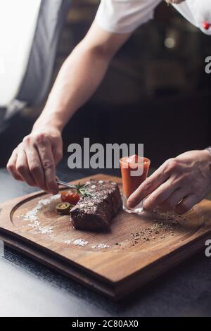 Der männliche Koch serviert köstliche Steaks auf dem Schneidebrett im Straßencafé Stockfoto