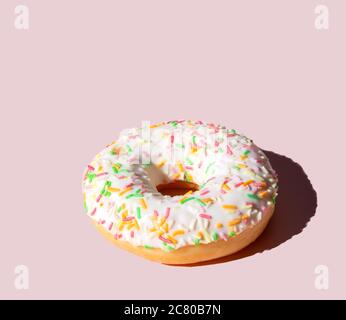 Donut mit weißem Zuckerguss und bunten Zuckerstäbchen.auf einem rosa Hintergrund Stockfoto