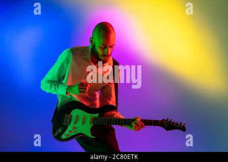 Gespannt. Junge kaukasische inspirierte und expressive Musiker, Gitarrist auf bunten Hintergrund in Neon. Konzept der Musik, Hobby, Festival, Kunst. Fröhliche Künstler, bunt, helles Porträt. Stockfoto