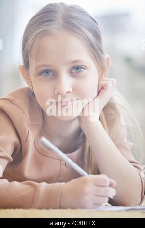 Vorderansicht Porträt von niedlichen blonden Mädchen lächeln an der Kamera während des Studiums zu Hause, verschwommen Bild durch Sonnenlicht beleuchtet Stockfoto
