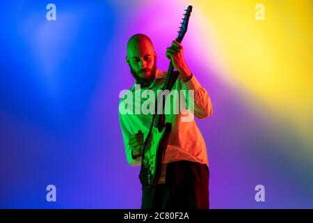 Gespannt. Junge kaukasische inspirierte und expressive Musiker, Gitarrist auf bunten Hintergrund in Neon. Konzept der Musik, Hobby, Festival, Kunst. Fröhliche Künstler, bunt, helles Porträt. Stockfoto