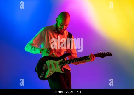 Gespannt. Junge kaukasische inspirierte und expressive Musiker, Gitarrist auf bunten Hintergrund in Neon. Konzept der Musik, Hobby, Festival, Kunst. Fröhliche Künstler, bunt, helles Porträt. Stockfoto