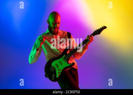 Gespannt. Junge kaukasische inspirierte und expressive Musiker, Gitarrist auf bunten Hintergrund in Neon. Konzept der Musik, Hobby, Festival, Kunst. Fröhliche Künstler, bunt, helles Porträt. Stockfoto