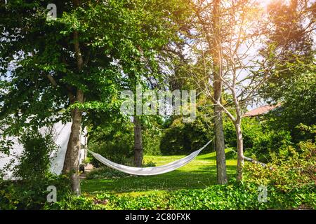 Weiße Hängematte in einem grünen Garten in der Sommerzeit zwischen zwei Bäumen Stockfoto