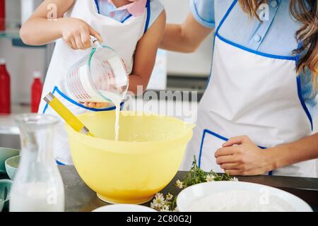 Mutter und Tochter in Schürze Gießen warme Milch in Schüssel, wenn Keksteig Stockfoto