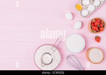 Draufsicht auf Produkte zum Backen von köstlichem Erdbeerkuchen, gesiebenem Mehl, Eiern, Zucker und frischen Beeren auf einem rosafarbenen Tisch. Stockfoto