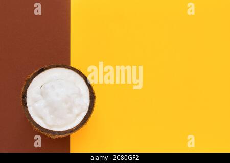 Frisches Kokosöl in der Hälfte der Nuss auf einem hellgelb-braunen Hintergrund. Draufsicht, Kopierbereich für Text. Stockfoto