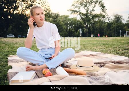 Schönes Teenager-Mädchen auf karierten sitzen und nachdenklich Musik in den Kopfhörern auf Picknick im Park hören Stockfoto