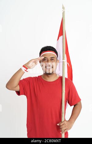 asiatischer Mann, der der Kamera einen Gruß gibt, während er die indonesische Flagge auf weißem Hintergrund hält Stockfoto