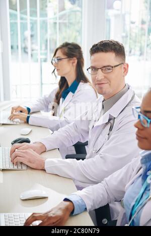 Lächelnd positiver junger Forscher, der mit seinen Kollegen am Computer arbeitet Stockfoto