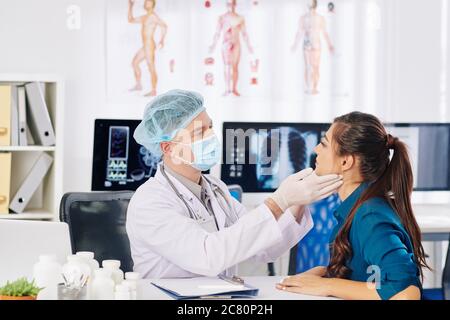 Allgemeinarzt in medizinischen Maske und Gummihandschuhe Überprüfung der Leisten der jungen Frau besucht ihn für die jährliche Check-up Stockfoto