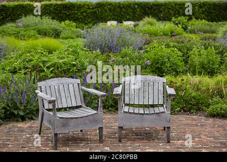 Zwei Holzgartenstühle auf gepflasterter Terrasse in der ummauerten Garten in Scampston Hall Stockfoto