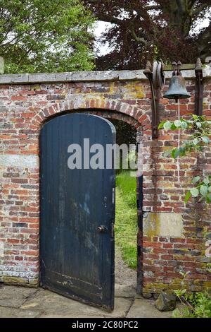 Alte Glocke im Mauerwerk des ummauerten Gartens bei Scampston Hall neben dem Holzeingang, der zum führt Capability Brown Parkland Area Stockfoto