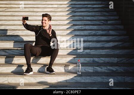 Junge gut aussehende sportliche Mann glücklich zeigt hallo hesture im Video-Chat auf Handy nach dem Training im Freien sprechen Stockfoto